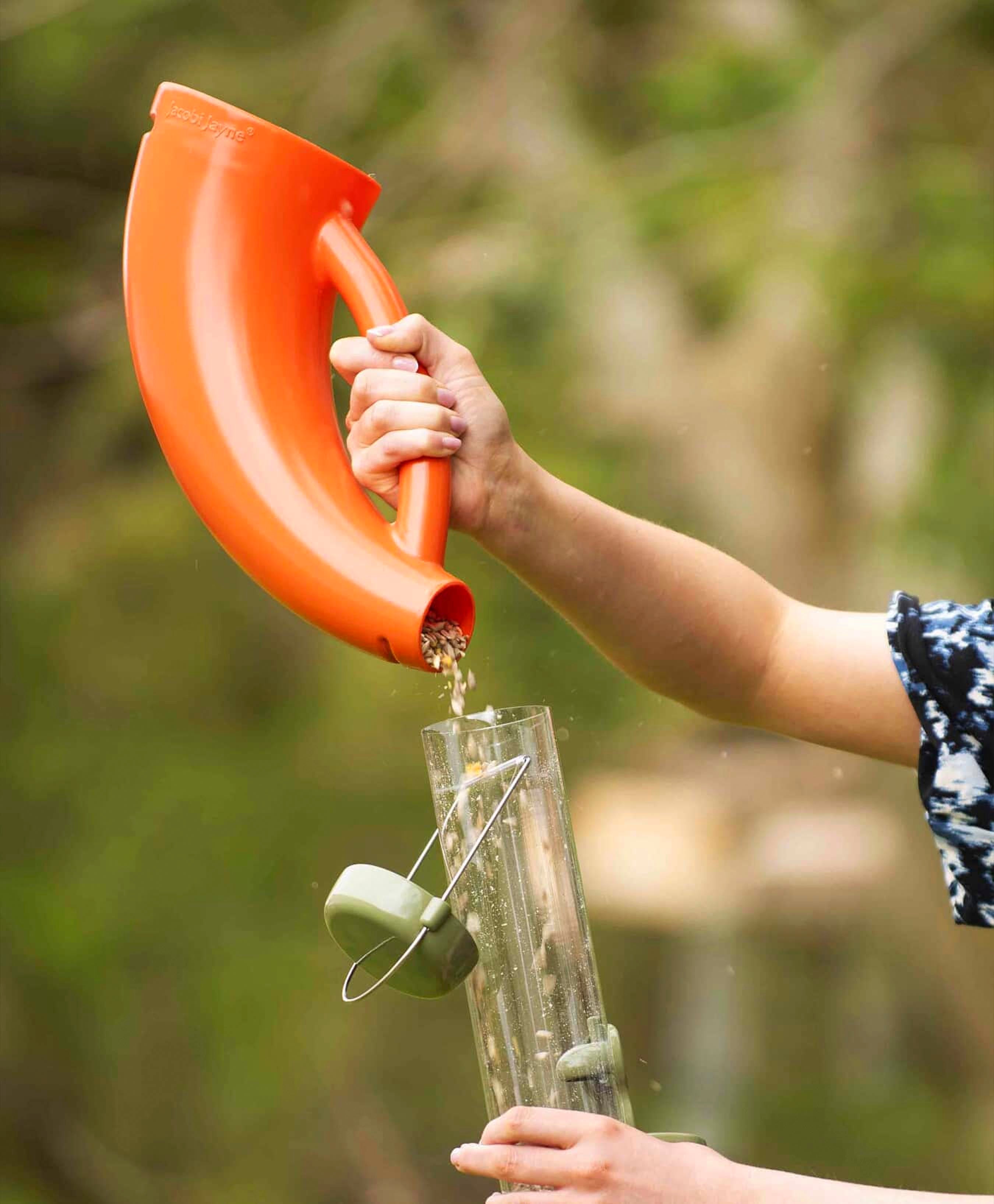 Vibrant orange bird food scoop pouring seed blends and mixes into durable, large metal seed bird feeder. 